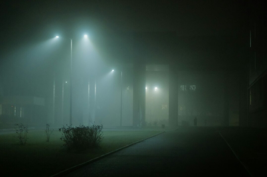 Distant anonymous figure walking through fog on an empty street
